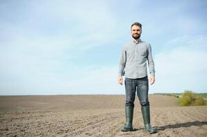 une agriculteur dans bottes travaux dans une champ semé dans printemps. un agronome des promenades le Terre, évaluer une labouré champ dans l'automne. agriculture. photo