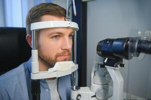 Beau Jeune homme est vérification le œil vision dans moderne ophtalmologie clinique. patient dans ophtalmologie clinique photo