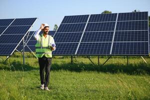 un Indien Masculin ingénieur dans une vert gilet est travail sur une champ de solaire panneaux. le concept de renouvelable énergie. photo