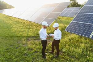 le solaire ferme solaire panneau avec deux ingénieurs marcher à vérifier le opération de le système, alternative énergie à conserver le du monde énergie, photovoltaïque module idée pour nettoyer énergie production photo