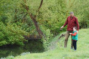 une père enseignement le sien fils Comment à poisson sur une rivière à l'extérieur dans été ensoleillement photo