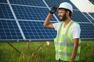 un Indien Masculin ingénieur dans une vert gilet est travail sur une champ de solaire panneaux. le concept de renouvelable énergie. photo