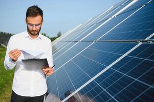 homme dans blanc chemise permanent près photovoltaïque panneaux sur ensoleillé journée dans campagne photo