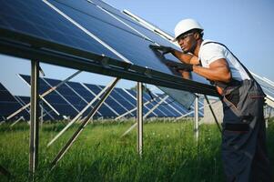 portrait de africain américain électricien ingénieur dans sécurité casque et uniforme installation solaire panneaux. photo