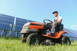 une homme tond le herbe près le solaire panneaux. vert énergie photo