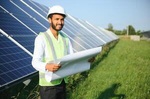 un Indien Masculin ingénieur dans une vert gilet est travail sur une champ de solaire panneaux. le concept de renouvelable énergie. photo