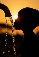 ai généré Jeune garçon les boissons l'eau de robinet pendant le coucher du soleil photo