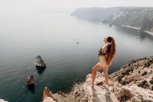 femme Voyage mer. content touristique prendre plaisir prise image en plein air pour souvenirs. femme voyageur regards à le bord de le falaise sur le mer baie de montagnes, partage Voyage aventure périple photo