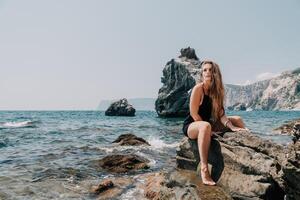 femme été Voyage mer. content touristique dans chapeau prendre plaisir prise image en plein air pour souvenirs. femme voyageur posant sur le plage à mer entouré par volcanique montagnes, partage Voyage aventure périple photo