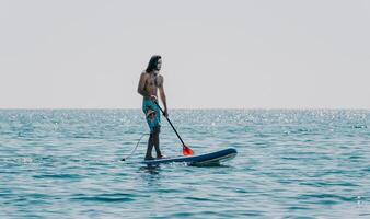 homme souper mer. fort athlétique homme apprend à pagayer souper permanent sur planche dans ouvert mer océan sur ensoleillé journée. été vacances vacances et Voyage concept. aérien voir. lent mouvement photo