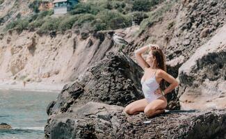 femme Voyage mer. content touristique dans blanc bikini prendre plaisir prise image en plein air pour souvenirs. femme voyageur posant sur le plage à mer entouré par volcanique montagnes, partage Voyage aventure périple photo