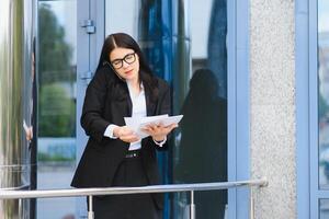 femme d'affaires avec téléphone près du bureau. portrait d'une belle femme souriante dans des vêtements de bureau de mode parlant au téléphone tout en se tenant à l'extérieur. communication téléphonique. image de haute qualité. photo