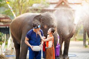 Jeune femme vaisselle thaïlandais traditionnel robe s'applique poudre à une Jeune homme joue sur un l'éléphant éclabousser l'eau Contexte à Songkran festival. photo