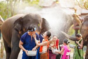 Jeune femme vaisselle thaïlandais traditionnel robe s'applique poudre à une Jeune homme joue sur un l'éléphant éclabousser l'eau Contexte à Songkran festival. photo