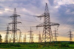 électricité pylônes palier le Puissance la fourniture à travers une rural paysage. Orange le coucher du soleil. sélectif se concentrer. photo