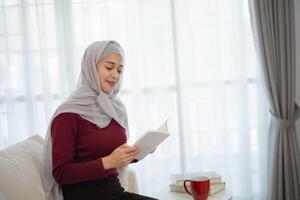 musulman Islam femme portant hijab ou gris écharpe est en train de lire une livre. elle est souriant et elle est profiter sa en train de lire photo