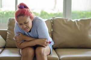 Jeune asiatique femme a menstruel crampes ou estomac douleur de autre causes. elle est assis sur le canapé. photo