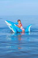 content fille de européen apparence âge de sept nager sur un gonflable gros requin jouet dans le mer.famille été vocation concept. verticale photo. photo
