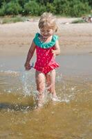 Jeune content enfant fille de européen apparence âge de 4 ayant amusement dans l'eau sur le plage et éclaboussures,tropical été vocations,vacances.a enfant jouit le mer.vertical photo. photo