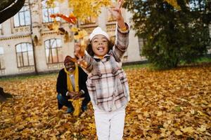 grand-père et petite-fille noirs se moquant des feuilles tombées dans le parc d'automne photo