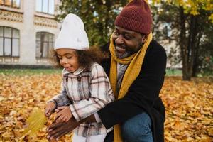 grand-père et petite-fille noirs se moquant des feuilles tombées dans le parc d'automne photo