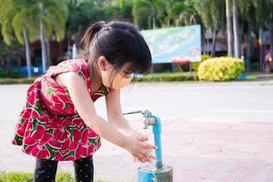 Une jolie petite fille portant un masque en tissu se lave les mains avec de l'eau propre du robinet dans l'espace public après avoir fait son activité. enfant de 4 ans. prévenir la propagation de la maladie du coronavirus covid 19.