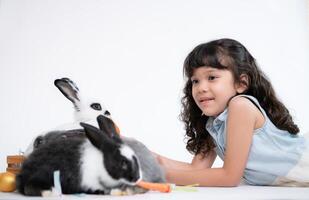 souriant peu fille et avec leur bien-aimée duveteux lapin, mettant en valeur le beauté de relation amicale entre humains et animaux photo