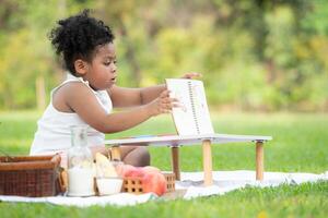 content famille profiter une pique-nique dans le parc, fille sont ayant amusement dessin sur papier mis sur le tableau. photo