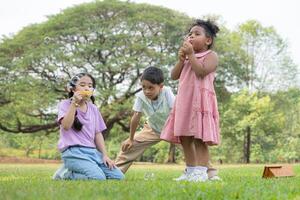 les enfants séance dans le parc avec soufflant air bulle, entouré par verdure et la nature photo