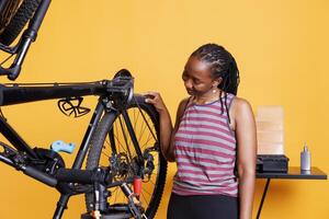 dévoué noir femme vérification vélo pneus pour dégâts à réparer avec professionnel travail outils. actif africain américain femelle travail sur cassé bicyclette caoutchouc roue avec spécialisé équipement. photo