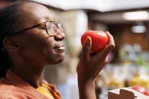 sélectif concentrer sur un africain américain femme à éco amical marché, admiratif frais, biologique produire. soucieux de leur santé, femelle client inhale Naturel senteurs, justificatif local, durable les pratiques. photo