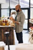 milieu est homme remplissage en haut une marron papier sac avec Orange Lentilles. Jeune homme verser céréales dans sac, achat en bonne santé des biens de réutilisable conteneurs avec biologique masse des produits. photo