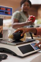 à le comptoir, un africain américain la caissière pèse localement grandi aubergine pour une femelle client. une commerçant les usages une numérique échelle à peser une fraîchement récolté bio légume. photo