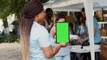 un isolé chromakey modèle pour humanitaire messages sur intelligent tablette est tenue par africain américain charité ouvrier. volontaire noir femme saisir numérique dispositif avec Vide vert écran afficher. photo