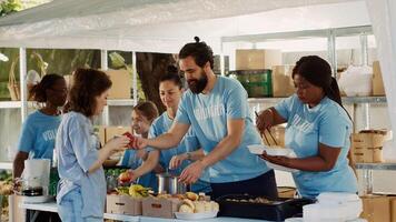 Jeune gens uni par engagement à charité, aider défavorisé et contribuant nourriture à personnes expérience sans-abrisme. bénévoles partage gratuit repas à le pauvres et nécessiteux. trépied tir. photo