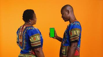 africain américain couple à la recherche à écran vert sur téléphone mise en page, en utilisant isolé chromakey modèle sur afficher. homme et femme montrer du doigt à Vide fond maquette mobile téléphone filtrer. photo