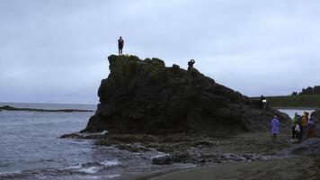 homme des stands sur Roche sur rivage. agrafe. groupe de gens sur rivage avec Roche sur nuageux journée. mer Roche avec groupe de touristes sur côte photo