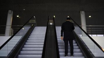 passager équitation sur le escalier mécanique en haut à le station de le sol métro. médias. arrière vue de une Jeune homme d'affaire sur le escalier mécanique. photo