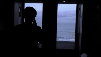 Jeune touristique avec une téléphone intelligent regards en dehors de le fenêtre de une en mouvement train. Stock agrafe. arrière vue de une Masculin silhouette parlant sur téléphone dans train. photo