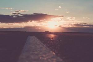 le coucher du soleil ou l'aube du soleil sur une route qui s'éloigne. les rayons du soleil se frayant un chemin à travers les nuages au-dessus de la route. photo