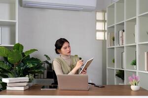 femme asiatique Créatif dans Accueil Bureau et portable pour recherche dans éloigné travail, social médias ou Blog dans appartement. free-lance à bureau avec ordinateur l'écriture e-mail, site Internet Publier et en ligne bavarder dans maison photo