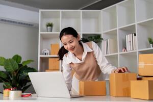 Jeune femme travail en ligne commerce électronique achats à sa magasin. Jeune femme vendeur préparer parcelle boîte de produit pour livrer à client. en ligne vente, commerce électronique. vente des produits en ligne photo