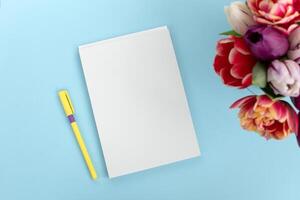 Haut vue de une bleu table avec une maquette de Vide des cahiers avec une bouquet de tulipes sur le côté. photo