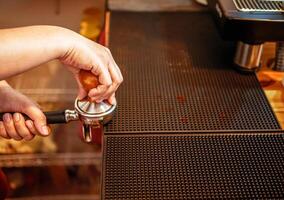 main de une barista en portant une porte-filtre et une café altérer fabrication un Expresso café. barista presses sol café en utilisant une altérer dans une café magasin photo