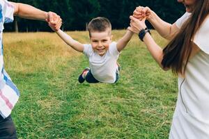 mather et père lancement peu fils en haut dans le air. famille temps ensemble. content peu garçon ayant amusement avec le sien maman et papa en plein air photo