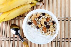 Naturel yaourt avec fait maison granola et des noisettes dans céramique bol sur une table Haut vue photo