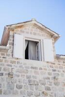 blanc ouvert volets dans le grenier de un vieux pierre maison contre une bleu ciel photo