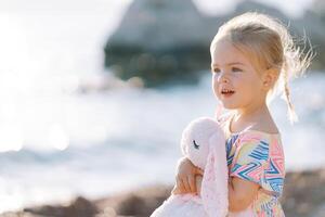 peu surpris fille des stands sur le plage étreindre une jouet lièvre photo