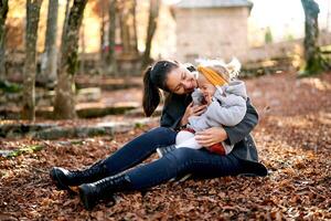 souriant mère chatouillement peu fille sur sa tour tandis que séance sur déchue feuilles dans le parc photo