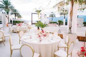 de fête les tables avec bouquets de fleurs et blanc chaises supporter près une étape décoré avec guirlandes de lumière ampoules photo